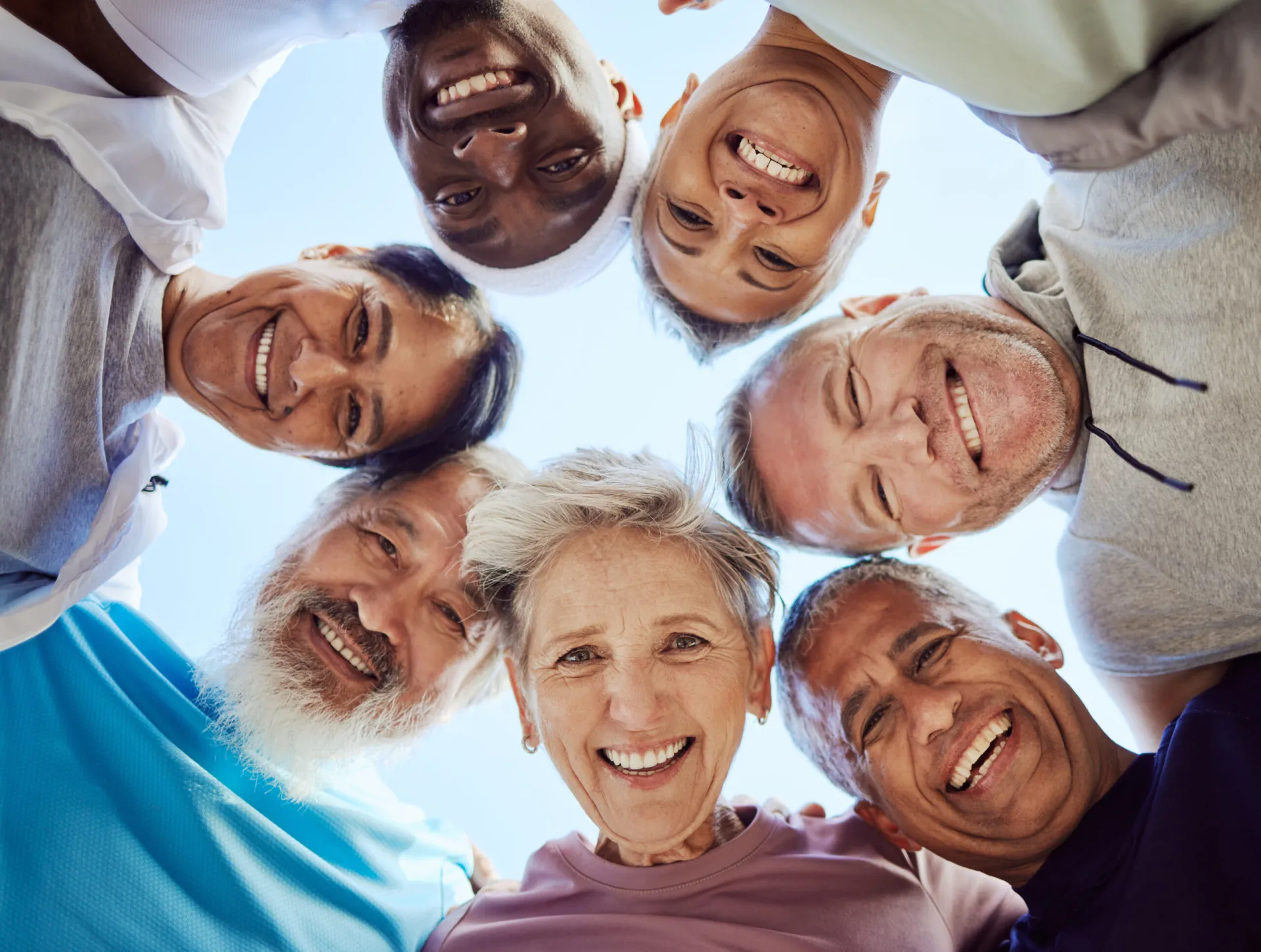 A group of seven people of various ages and backgrounds stand in a circle, smiling and looking down at the camera against a bright sky, celebrating their shared journey with food sensitivity testing.